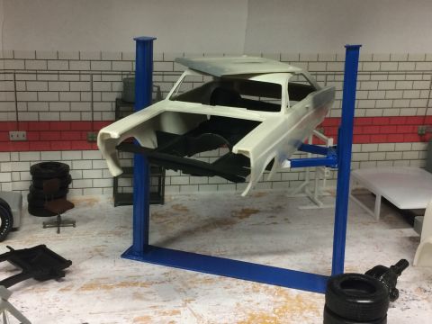 1989 Ford Bronco - Model car body is elevated on a lift in a workshop diorama.