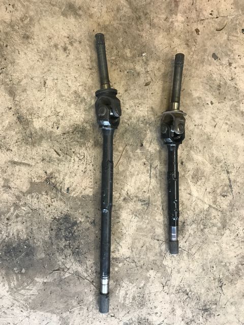 1996 Ford Bronco - Two drive axles are laid out on a concrete surface, showing their U-joint assemblies.