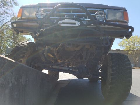 1988 Ford Bronco - Front view of a heavily modified truck with a winch and off-road tires, appearing to be from the early 1980s.