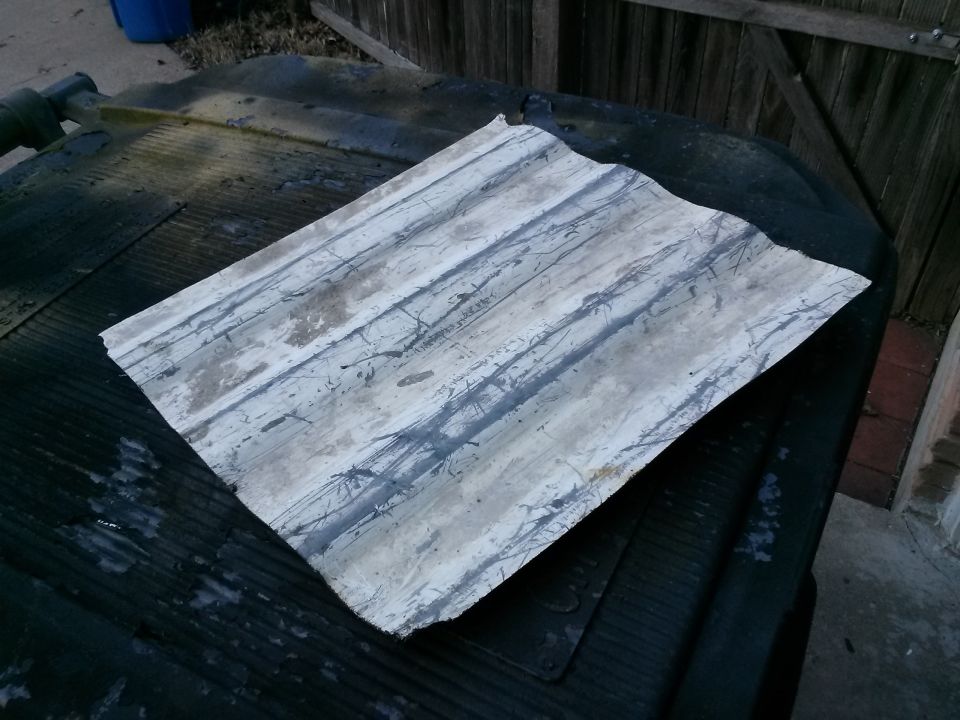 Corrugated metal sheet with grey and white paint splatters on a dark ribbed surface