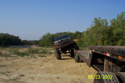 1979 Ford Bronco - A heavily modified truck is loaded onto a flatbed trailer in a sandy, outdoor area.