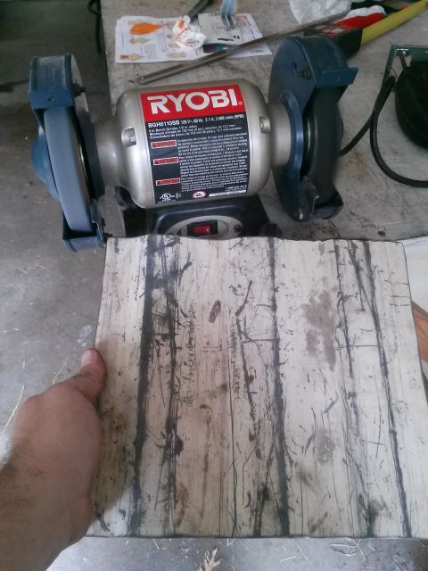 1996 Ford Bronco - A Ryobi bench grinder sits on a workbench next to a piece of wood being held by a hand.