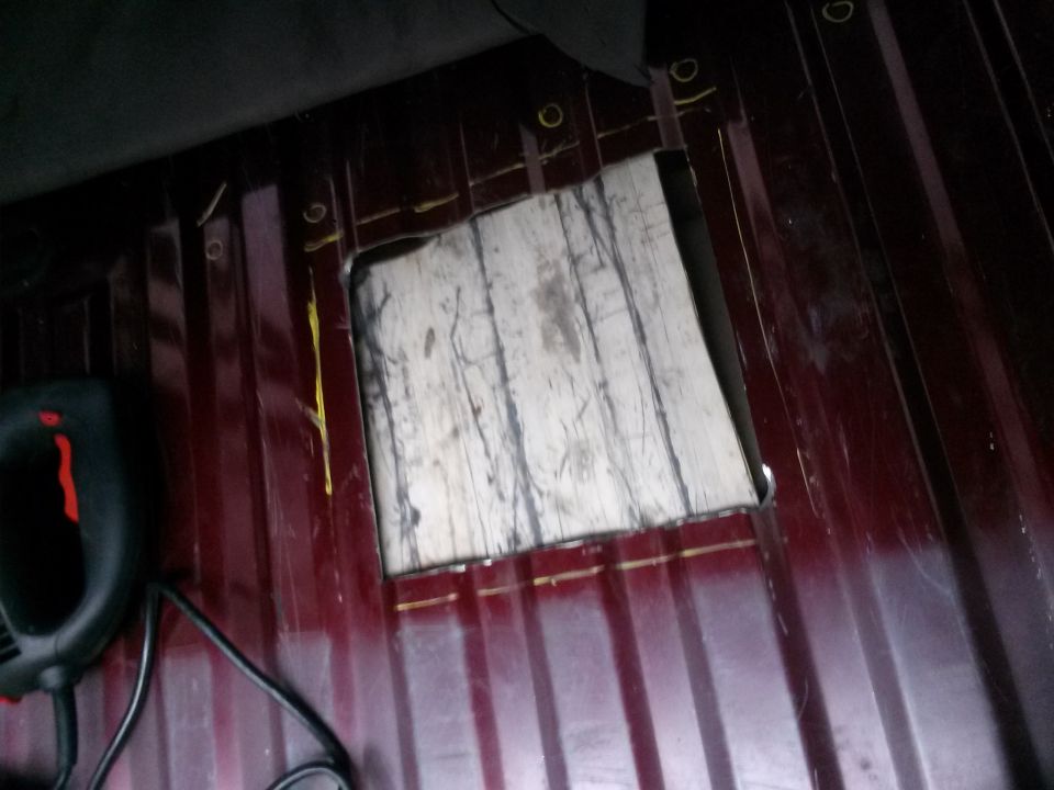 Maroon interior floor panel with a rectangular cut-out and visible tool. Supermotors.net logo in lower right