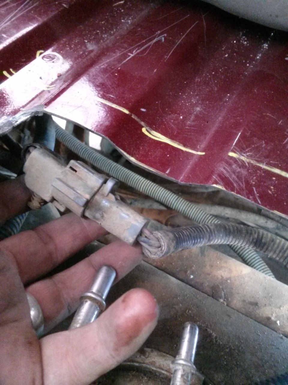 hand holding a disconnected fuel line connector with wires nearby