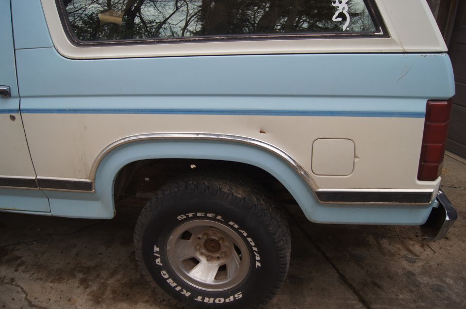 Side view of a light blue and white Ford Bronco, showing the rear wheel and fuel door