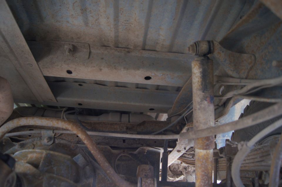 Undercarriage of a rusty vehicle showing suspension components and exhaust pipes