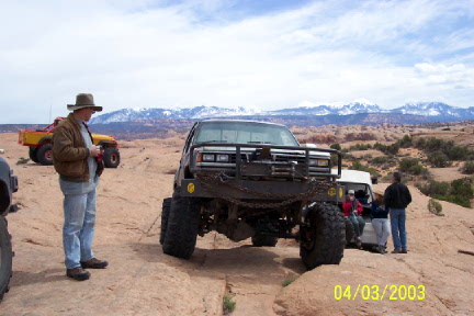 1979 Ford Bronco - A heavily modified off-road truck with a prominent bull bar and chains is seen in a desert landscape with mountains in the background.