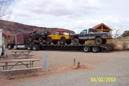 1979 Ford Bronco - Semi-truck trailer carrying three off-road vehicles and a pickup truck in a desert landscape.