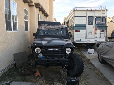 1987 Suzuki Samurai - A Suzuki Samurai is parked in a driveway with its front end elevated on a jack, next to a recreational vehicle.