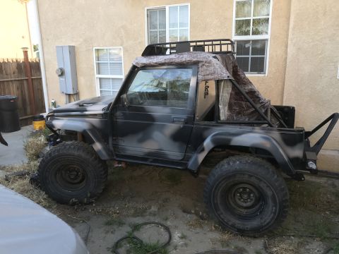 1987 Suzuki Samurai - Side view of a modified Suzuki Samurai with camouflage paint and off-road tires.