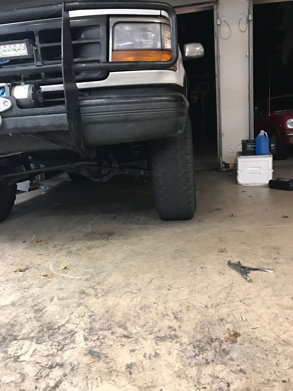 Front of a white Ford truck with a brush guard and light bar. The front tire and suspension are visible