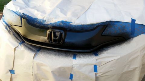 2015 Honda Fit - A black Honda grille is being spray painted, with masking tape and paper protecting the surrounding area.