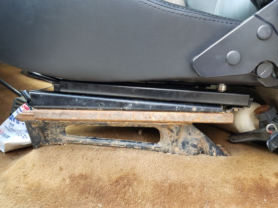 Seat mounting bracket with rust and dirt, under a black seat