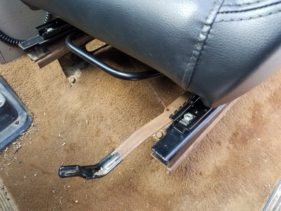 Close-up of a black leather seat base and its metal slider mechanism with a black adjustment lever on the floor