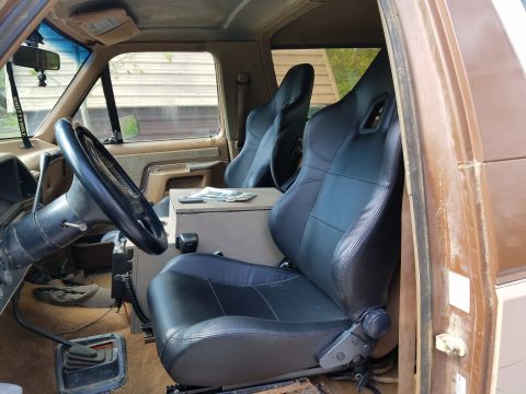 1988 Ford Bronco - The interior of a vehicle shows aftermarket bucket seats and a custom center console.