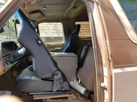 1988 Ford Bronco - The interior of a brown SUV shows removed seats and a cluttered cargo area, with a view of the dashboard and steering wheel.