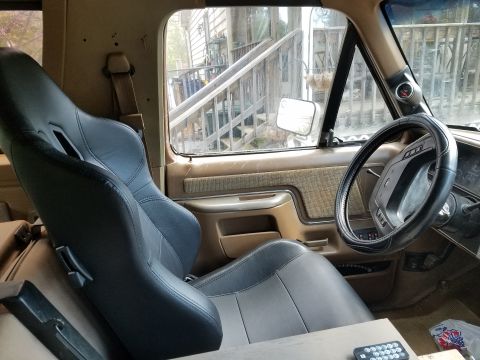 1988 Ford Bronco - The interior of a vehicle shows aftermarket racing seats and a steering wheel, with a gauge on the A-pillar.