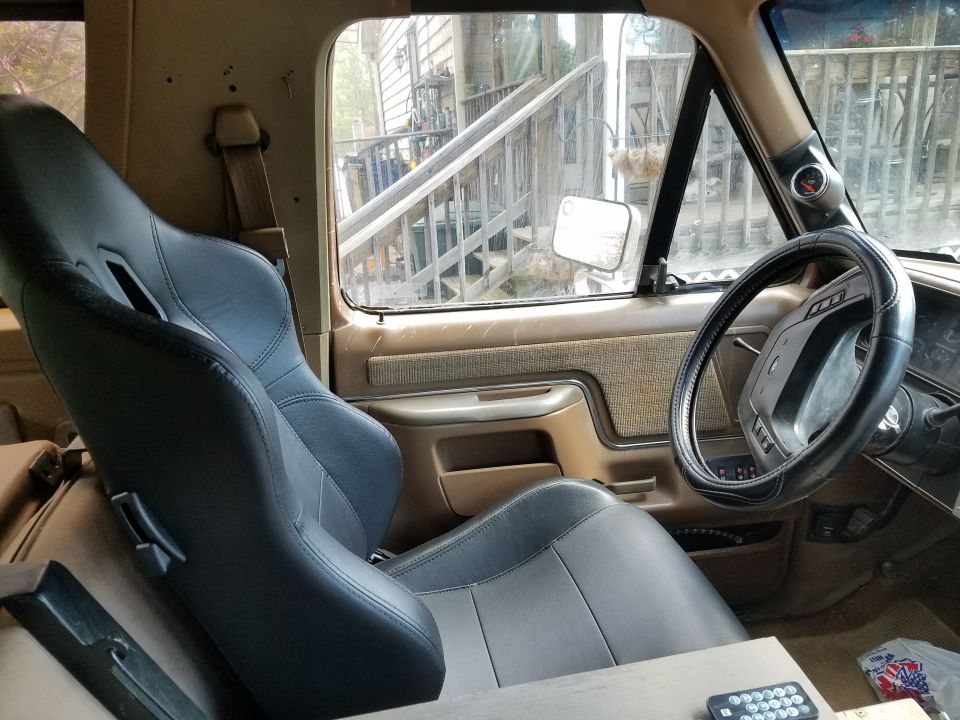 Interior of a tan and black vehicle with racing seats and a steering wheel. A gauge is mounted on the A-pillar