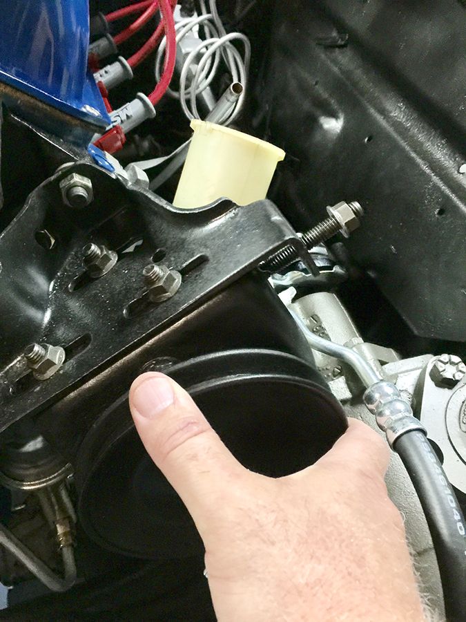 Hand pointing to a black engine component with visible bolts and hoses