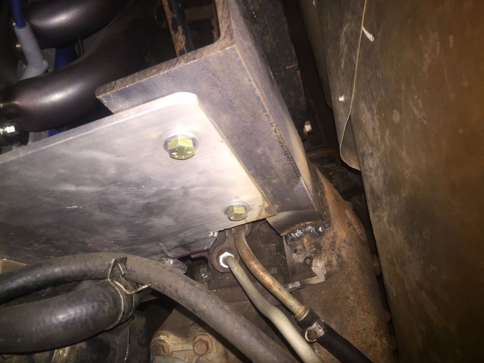 Close-up of engine bay with metal plates, bolts, and hoses visible