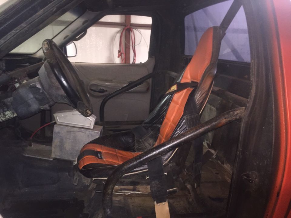 Interior view of a modified truck or SUV showing a racing seat, roll cage, and steering wheel