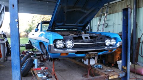 1971 Ford Ranchero - A blue pickup truck, possibly a 1970 model, is raised on a lift with its hood open, revealing the engine bay.