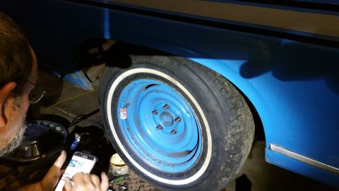 1971 Ford Ranchero - A person uses their phone while standing next to the wheel of a blue vehicle.
