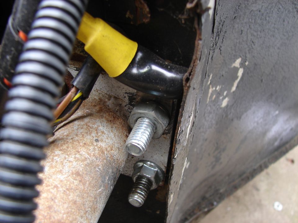 Close-up of rusty metal bracket with two bolts, electrical wiring, and corrugated tubing