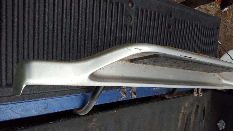 Silver running board with black textured step pad, resting on a blue surface against a black ribbed background