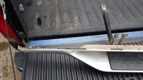 1994 Ford Bronco - Running board part with mounting hardware, placed inside a pickup truck bed.