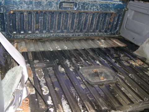 1994 Ford Bronco - The empty cargo bed of an older pickup, its blue-painted tailgate and corrugated steel floor heavily scratched, rusted and dusted with whit…