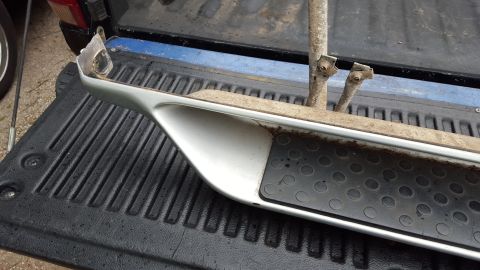 1994 Ford Bronco - Running board part with mounting brackets and grip pad, placed inside a pickup truck bed.