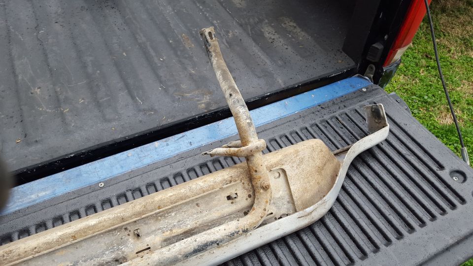 Rusty metal running board bracket with mounting holes, resting in a truck bed