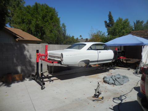 1966 Ford Fairlane - A white 1966 Ford Fairlane coupe is elevated on a lift for repairs in a driveway.
