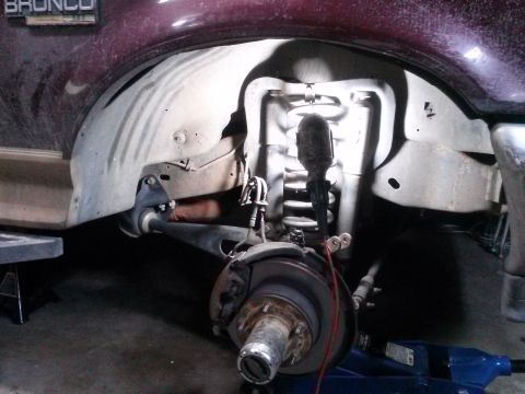 1996 Ford Bronco - Close-up view of the front suspension and wheel well of a maroon 1996 Ford Bronco.
