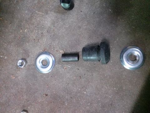 1996 Ford Bronco - Suspension parts including a bushing, sleeve, washers, and nut are displayed on a concrete surface.
