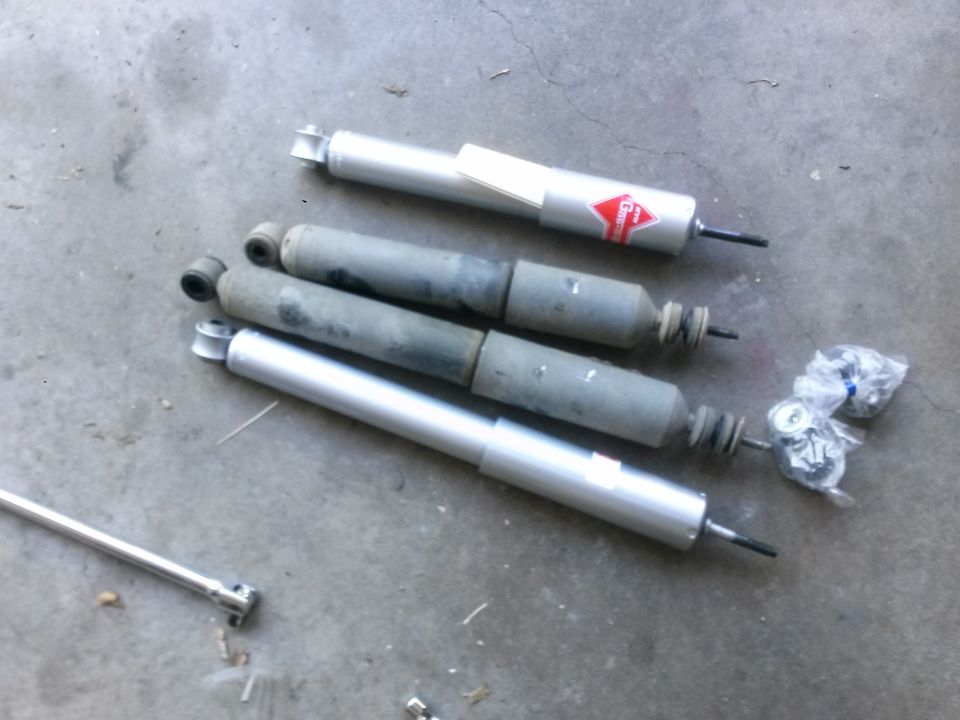 Four shock absorbers laid out on a concrete surface. One has a red and white logo