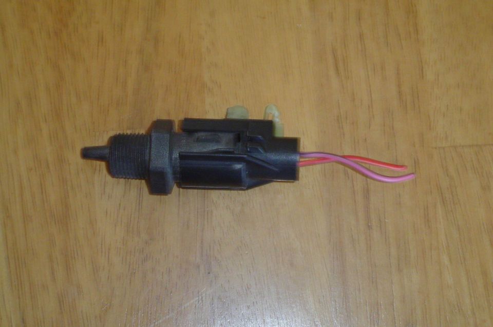Black threaded automotive sensor switch with two-pin connector and red pigtail wires on wood