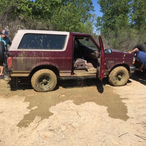1996 Ford Bronco - This maroon Ford Bronco is stuck in the mud, with people attempting to free it from the difficult terrain.