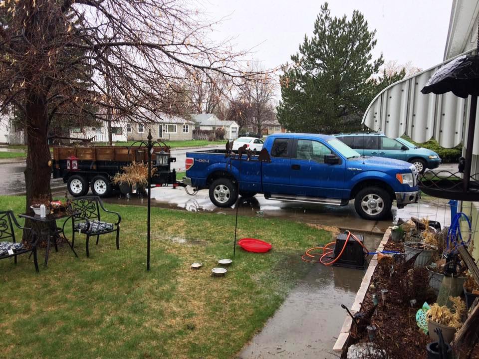 Blue Ford F-150 pickup truck with trailer parked in driveway, other vehicles visible