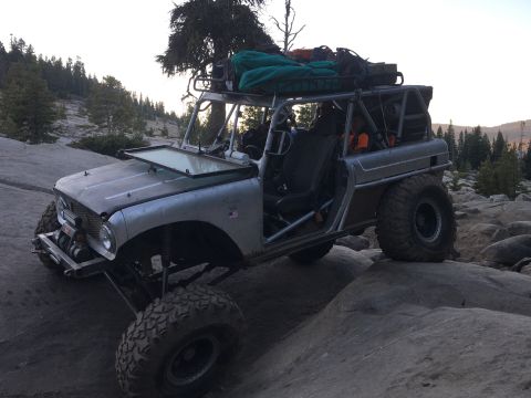 1961 International Scout 800 - Modified 1961 International Scout 800 navigates a rocky trail, equipped for off-road adventure with a roof rack and heavy-duty tires.