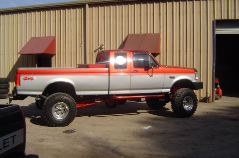 1993 Ford Bronco - This lifted pickup truck has a two-tone paint scheme and is parked in front of a corrugated metal building.