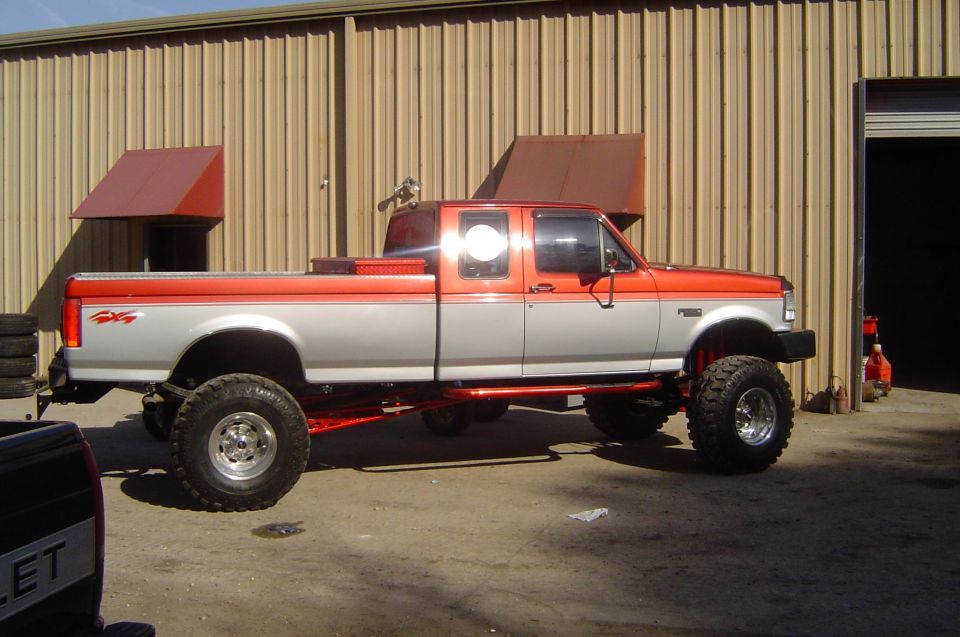 Lifted orange and silver Ford extended-cab pickup on mud tires