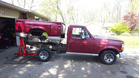 1994 Ford Bronco - A disassembled red Ford F-Series truck sits in a driveway, with its bed removed and supported by a red stand.