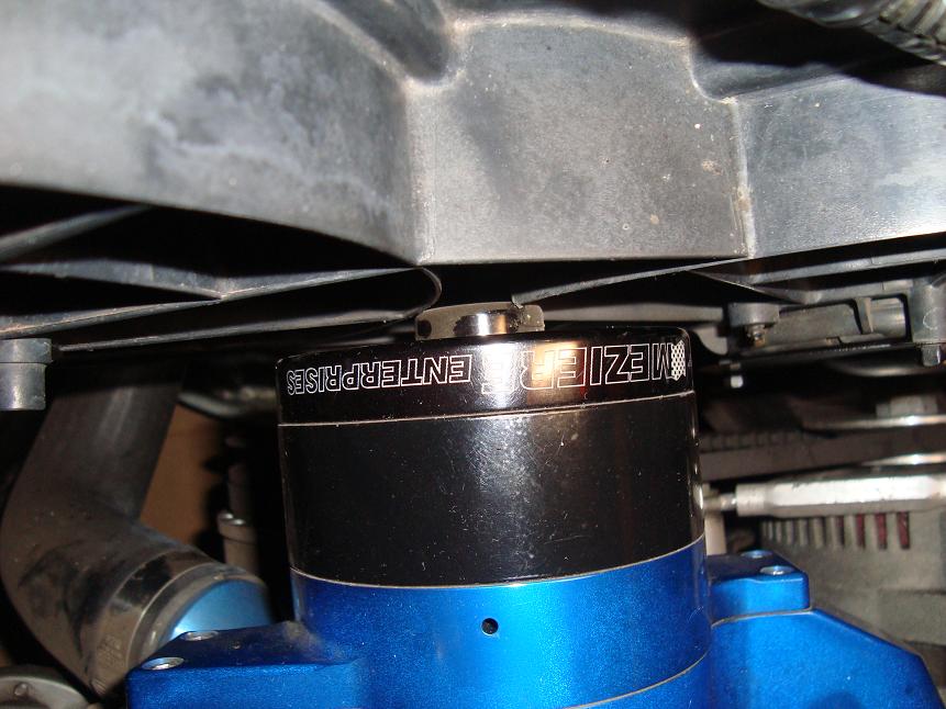 Meziere electric water pump with black motor and blue housing installed under a fan shroud in an engine bay