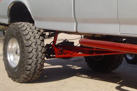 1993 Ford Bronco - Close-up of a lifted truck's suspension system, large off-road tires and custom red components.