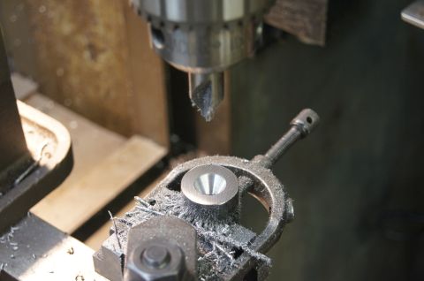 1979 Ford Bronco - A metal part is being machined on a drill press, with metal shavings accumulating around the workpiece.
