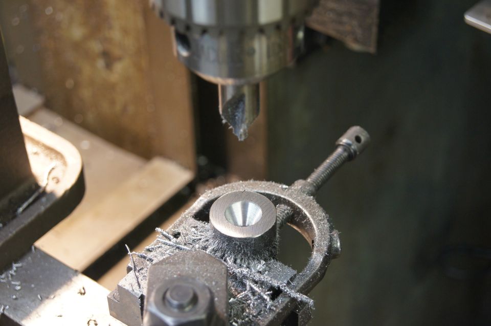 Machined metal part with conical recess on a drill press