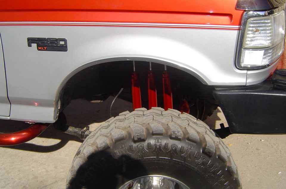 Lifted red-and-silver Ford F-250 XLT fender showing three red shocks per front wheel and a mud-terrain tire