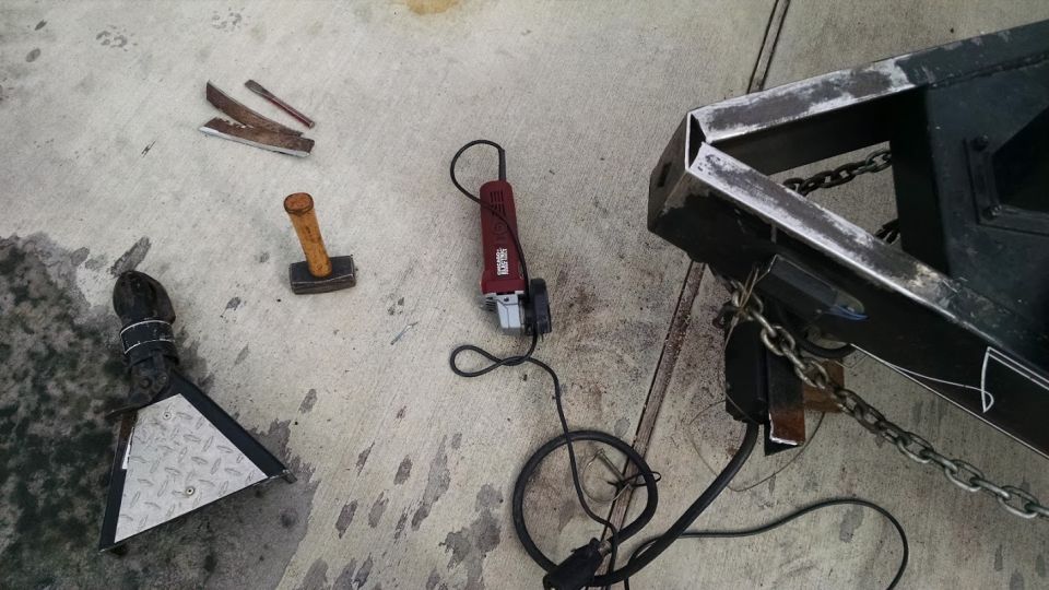 Trailer frame, angle grinder, hammer, and chisels on concrete